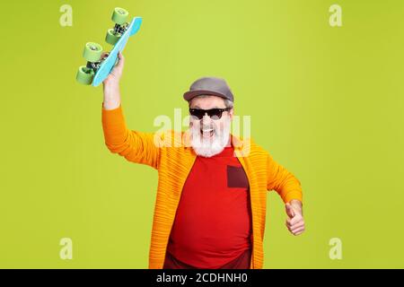 Homme patineur. Portrait de l'homme hipster senior dans des lunettes à la mode isolées sur fond vert de studio. Concept de mode de vie technologique et joyeux pour les personnes âgées. Couleurs tendance, toujours jeune. CopySpace pour votre annonce. Banque D'Images