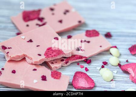 Barre entière en chocolat rose décorée de tranches de fruits à coque et de tranches sur fond gris. Chocolat artisanal tendance. Idée cadeau. Banque D'Images