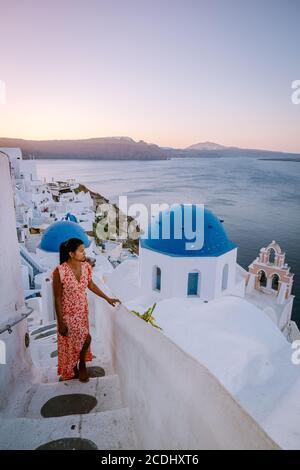 Santorini Grèce, jeune femme en vacances de luxe à l'île de Santorini regardant le lever du soleil près de l'église à dôme bleu et le village blanchi à la chaux d'Oia Banque D'Images