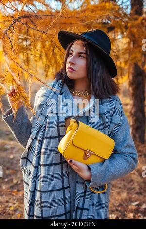 Mode d'automne. Femme en chapeau portant des vêtements élégants et tenant un sac à main jaune dans le parc. Vêtements et accessoires Banque D'Images
