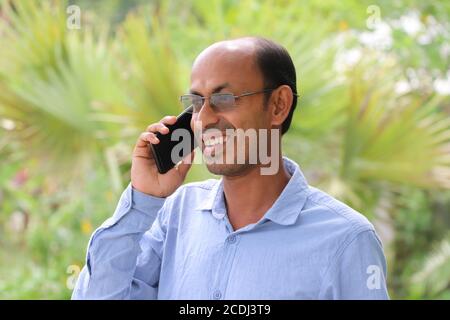 Homme asiatique souriant parlant sur un téléphone mobile à l'extérieur dans un stationnement Banque D'Images