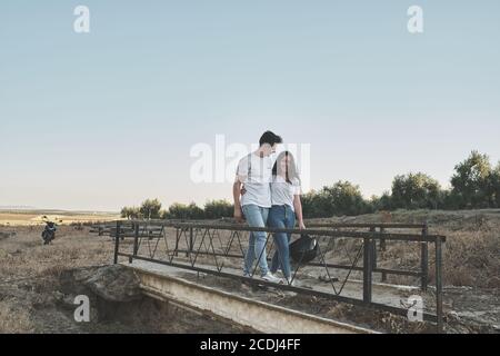 couple marchant sur un vieux pont avec leur moto garée derrière Banque D'Images