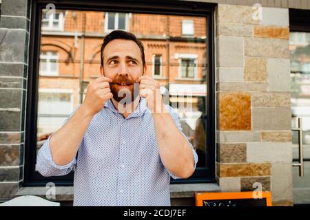 Homme d'âge moyen touchant la moustache tout en souriant dans la rue Banque D'Images