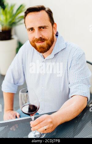 Homme aux cheveux rouges avec moustache assis à la table avec du verre de vin rouge Banque D'Images