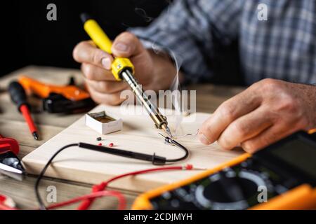 Un électricien avec fer à souder électrique répare le multimètre. Les gens au travail. Technologie. Banque D'Images