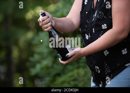 Une femme ouvre une bouteille de champagne à un fête de remise des diplômes Banque D'Images