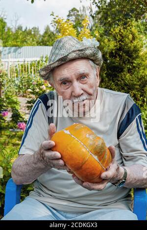 vieux dans un chapeau avec une citrouille dans le jardin. jardinier tient une citrouille orange mûre. concept de vieillesse active Banque D'Images