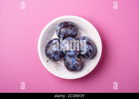 Fruits prune mûrs frais dans un bol en bois blanc sur fond rose minimal, vue du dessus Banque D'Images