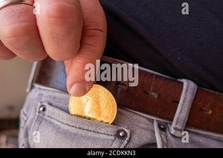 Une pièce de monnaie Bitcoin dorée est mise dans un pantalon gris poche Banque D'Images
