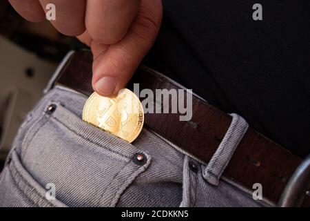 Une pièce de monnaie Bitcoin dorée est mise dans un pantalon gris poche Banque D'Images