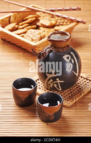 Ensemble de saké japonais composé d'une bouteille et de deux verres à liqueur sur un tapis de bambou Banque D'Images