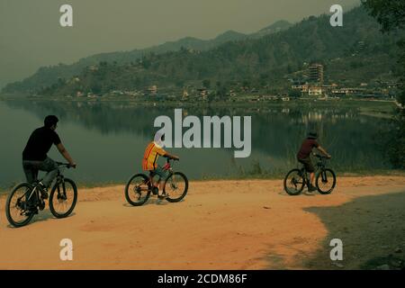 Une famille faisant du vélo le long du lac Phewa près de Pokhara dans le district de Kaski, Gandaki, Népal. Le lac Phewa est l'un des lacs qui se rétrécissent en Asie du Sud. Banque D'Images