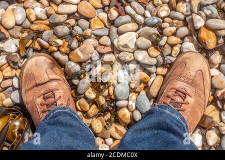 Une paire de pieds mâles en cuir marron fait sur une plage de galets. Banque D'Images