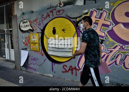 Ankara, Turquie. 29 août 2020. Un homme passe devant un graffiti représentant un émoji masqué au visage avec un œil clignotant dans le quartier de Cankaya. En Turquie, le nombre de décès quotidiens du coronavirus COVID-19 a atteint 36 le 28 août, atteignant le niveau le plus élevé depuis la mi-mai. Crédit : Altan Gocher/ZUMA Wire/Alamy Live News Banque D'Images