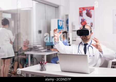 Médecin utilisant la technologie futuriste de réalité augmentée portant un casque dans le bureau de l'hôpital et une blouse blanche avec stéthoscope. Femme handicapée senior discutant avec medic dans le couloir de la clinique. Banque D'Images