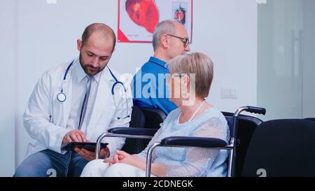 Médecin discutant du diagnostic et du traitement de rétablissement avec une femme âgée handicapée en fauteuil roulant. Vieil homme dans la salle d'attente de l'hôpital. Medic portant un stéthoscope et une couche blanche. Banque D'Images