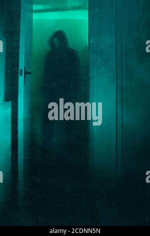 Un concept d'Halloween d'une figure à capuche floue effrayante, debout dans une porte. Avec un montage abstrait, vintage et poussiéreux. Banque D'Images