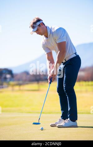 un golfeur de la vingtaine planifiant sa mise de tir à la épinglez un vert lors d'une journée ensoleillée Banque D'Images