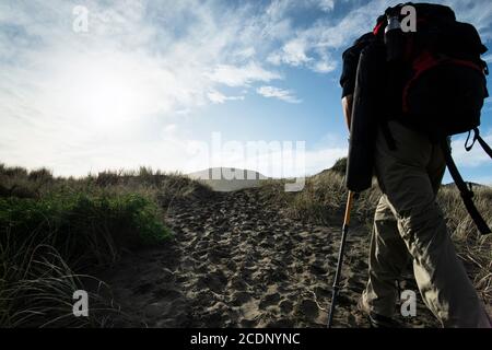 Un routard marchant sur la piste de sable vers la plage d'Anawhata, Auckland Banque D'Images