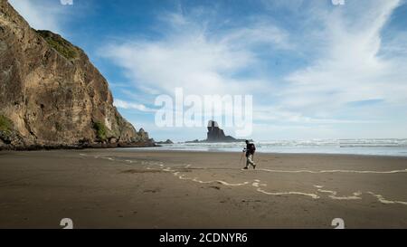 Un routard marchant sur la plage de sable noir d'Anawhata avec le rocher Keyhole au loin, Waitakere, Auckland Banque D'Images