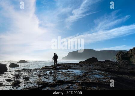 Un routard debout sur les rochers de la plage d'Anawhata, Waitakere, Auckland Banque D'Images