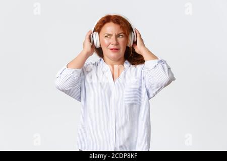 Emotions, style de vie et loisirs. Une femme d'âge moyen à tête rouge confuse et mécontente, ne comprend pas ce qui joue Banque D'Images