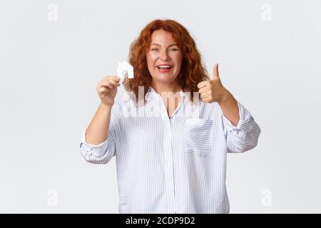 Louer, acheter des biens immobiliers et concept immobilier. Joyeuse et heureuse femme d'âge moyen à tête rouge montrant la carte de maison et les pouces vers le haut comme l'achat de la nouvelle maison Banque D'Images