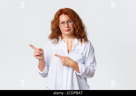 Sceptique et déçue redhead moyenne-âge mère, femme en lunettes scolding personne, pointant les doigts laissés à quelque chose de mauvais, regardant jugement Banque D'Images