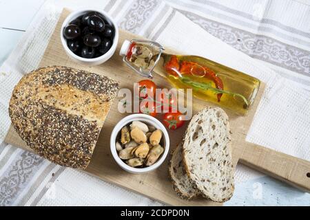 Olives noires et moules dans des bols en céramique, tomates fraîches, pain et bouteille d'huile d'olive aux épices Banque D'Images