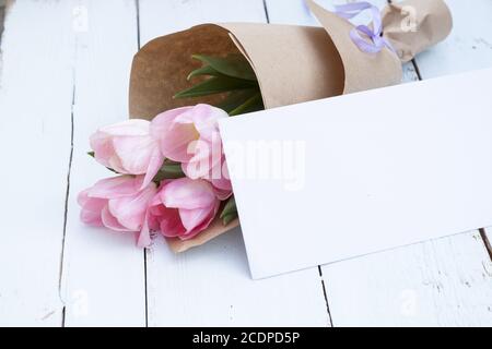 Beau bouquet de tulipes roses à côté d'une enveloppe blanche sur fond de bois clair Banque D'Images