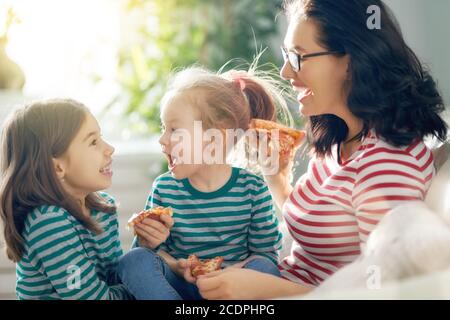 Bonne famille aimante. Mère et ses filles les filles mangent de la pizza sur le canapé de la chambre. Banque D'Images