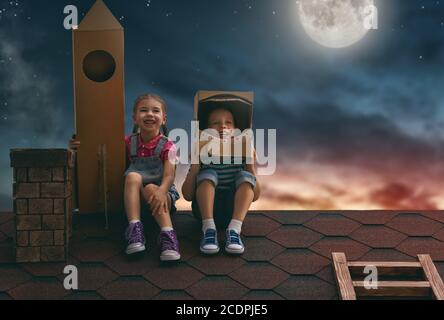 Deux petits enfants jouant aux astronautes. Enfants sur fond de ciel lunaire. Enfant garçon dans un costume d'astronaute et enfant fille avec un pied de fusée jouet Banque D'Images