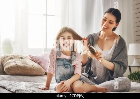 Famille heureuse et aimante. La mère se peigne les cheveux de sa fille, assis sur le lit dans la chambre. Banque D'Images