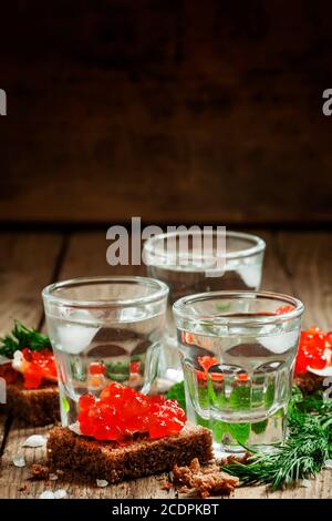 Vodka russe froide avec de la glace et des petits sandwiches en-cas avec du beurre et du caviar de saumon rouge sur une ancienne table en bois dans un style rustique, concentration sélective Banque D'Images