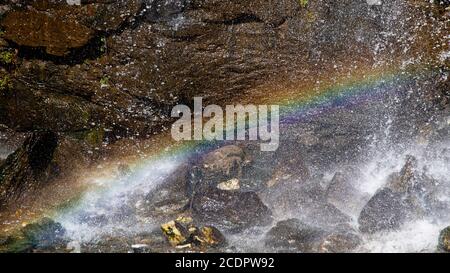 Un bel arc-en-ciel se forme sous une chute d'eau en raison de la lumière du soleil qui traverse des gouttelettes d'eau par une journée ensoleillée. Banque D'Images