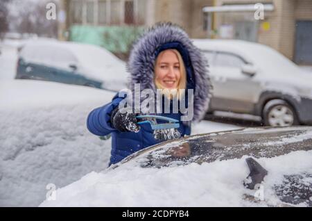 Défricher la neige de la voiture en hiver dans la cour avec une brosse Banque D'Images