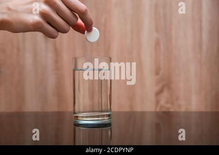 Main femelle tenant un comprimé effervescent rond sur un verre d'eau sur une table noire sur un fond clair. Espace de copie Banque D'Images