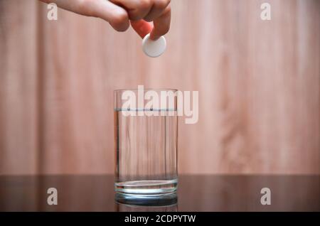 Main femelle tenant un comprimé effervescent rond sur un verre d'eau sur une table noire sur un fond clair. Espace de copie Banque D'Images