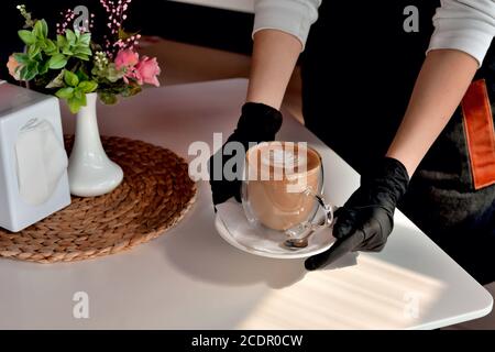 mains d'une serveuse en gants médicaux avec une tasse de café, dans un café, virus, en gros plan sur une pandémie de sécurité médicale Banque D'Images