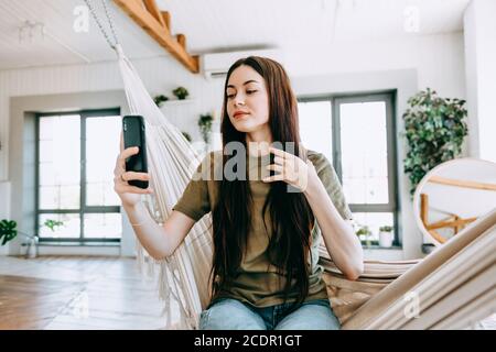 Belle jeune femme heureuse se relaxant dans la maison, faisant le selfie. Banque D'Images