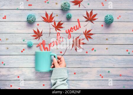 Étalages saisonniers d'automne avec feuilles d'érable et boules décoratives en rotin sur bois gris clair vieilli. Main tient tasse en céramique avec des mots Merci coupé de p Banque D'Images