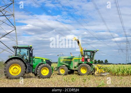 Allemagne agriculture agricole récolte du maïs sous des lignes et des pylônes haute tension Tracteur John Deere Banque D'Images