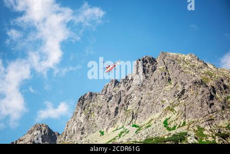 Hélicoptère volant dans les Hautes montagnes à la recherche de randonneurs et de touristes. Équipe de secours aidant le touriste qui a eu un accident. Banque D'Images