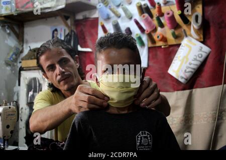 Gaza. 29 août 2020. Le tailleur palestinien Mohammed Awadallah ajuste un masque de visage fait par lui pour un garçon lors de son atelier au camp de réfugiés de Shati à Gaza, le 29 août 2020. Credit: Rizek Abdeljawad/Xinhua/Alamy Live News Banque D'Images