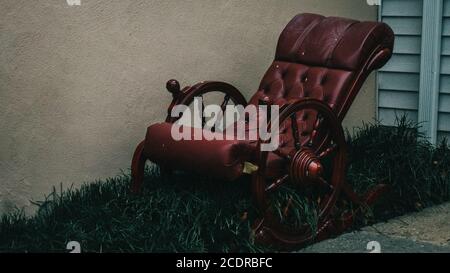 Une chaise berçante rouge à l'ancienne, ornée d'un amorti D'herbe à côté d'un bâtiment Banque D'Images