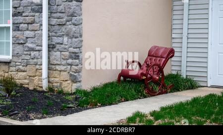 Une chaise berçante rouge à l'ancienne, ornée d'un amorti D'herbe à côté d'un bâtiment Banque D'Images
