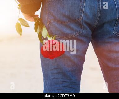 Homme avec une rose derrière son dos attendant l'amour. Romantique date sur la plage Banque D'Images