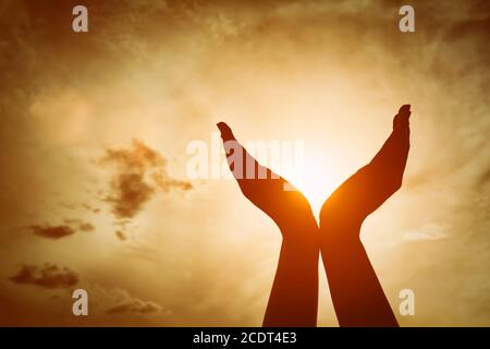 Mains levées prenant le soleil sur le ciel de coucher de soleil. Concept de spiritualité, de bien-être, d'énergie positive Banque D'Images