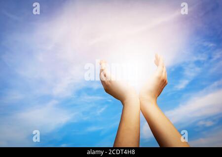 Mains levées prenant le soleil sur le ciel bleu. Concept de spiritualité, de bien-être, d'énergie positive Banque D'Images