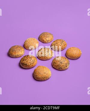 Pains à pain alignés symétriquement et isolés sur fond violet sans couture. Pains à hamburger à croûte dorée. Petits pains aux graines de sésame et de pavot. Banque D'Images